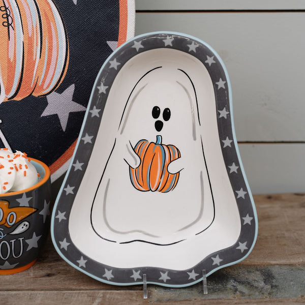 Halloween-themed plate with ghost design holding a pumpkin on a wooden surface.