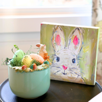 Decorative Easter scene with a small rabbit figurine, eggs, and a painted bunny card on a table.