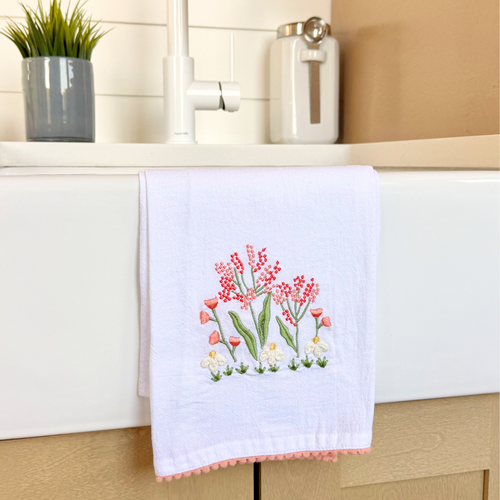 A white kitchen tea towel with a delicate pink wildflowers design and a small pink trim at the bottom edge.