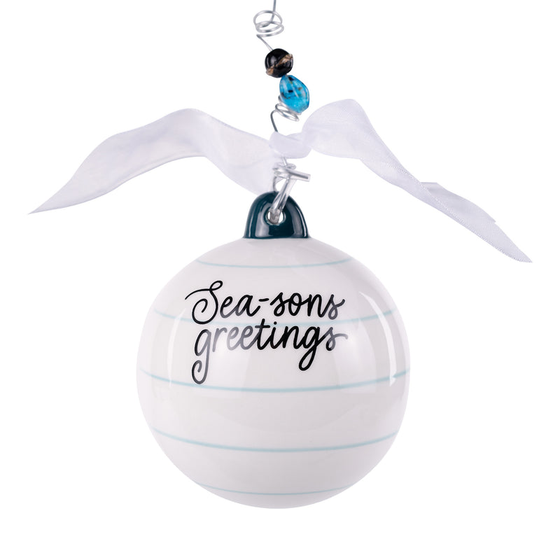 White ornament with 'Sea-sons greetings' text, ribbon, and beads on a white background