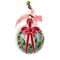 Decorative Christmas ornament with a red bow and green wreath design on a white background.