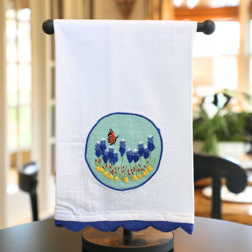 White towel with embroidered design of a butterfly and flowers on a stand.