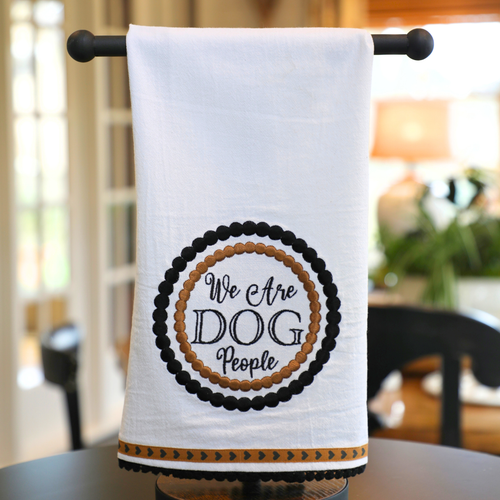 A white tea towel with a circular text design that reads 'We Are DOG People' surrounded by a black and beige patterned border.