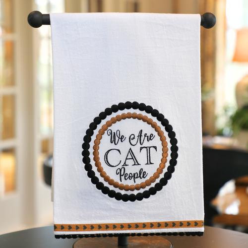 A white cotton tea towel with a circular text design that reads 'We Are CAT People' surrounded by a pattern of cat silhouettes in black and beige tones.