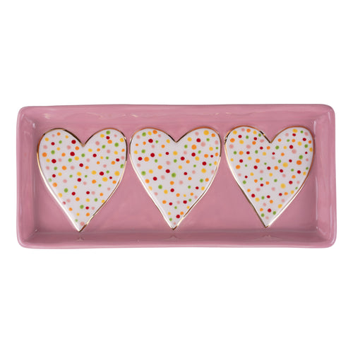 Rectangular pink tray with three heart-shaped polka dot cookies on a white background