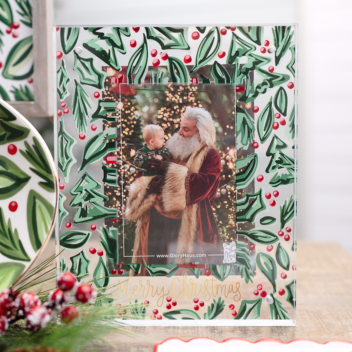 Christmas photo frame with Santa Claus holding a child against a holly leaf and berry pattern.