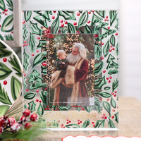 Christmas photo frame with Santa Claus holding a child against a holly leaf and berry pattern.