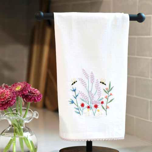 White towel with floral embroidery hanging on a rack, next to a vase of flowers.